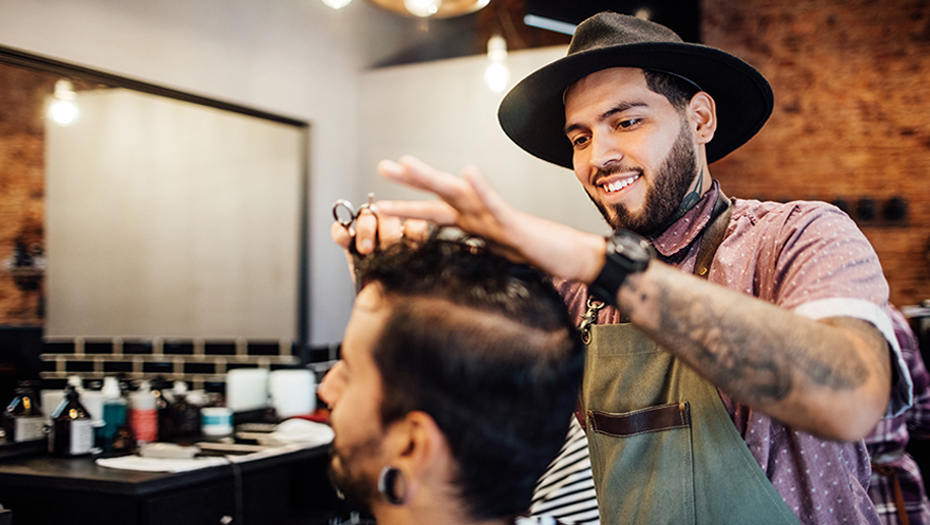 Hairstylist talking and looking at a client’s phone while the client is sitting down, getting ready for a haircut.