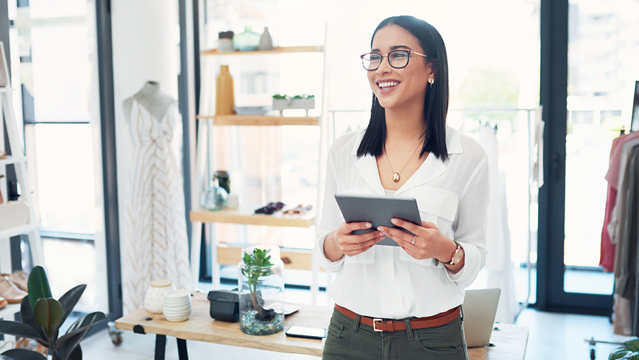 Female small business owner standing in her coffee shop, looking at her iPad.